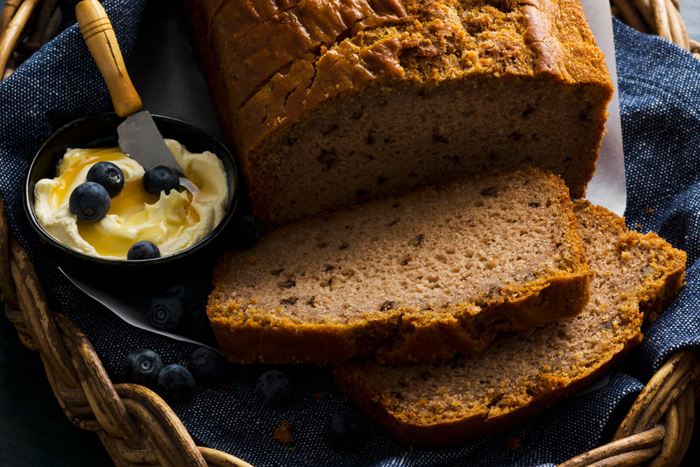 Slices of banana bread next to a bowl of cream and blueberries