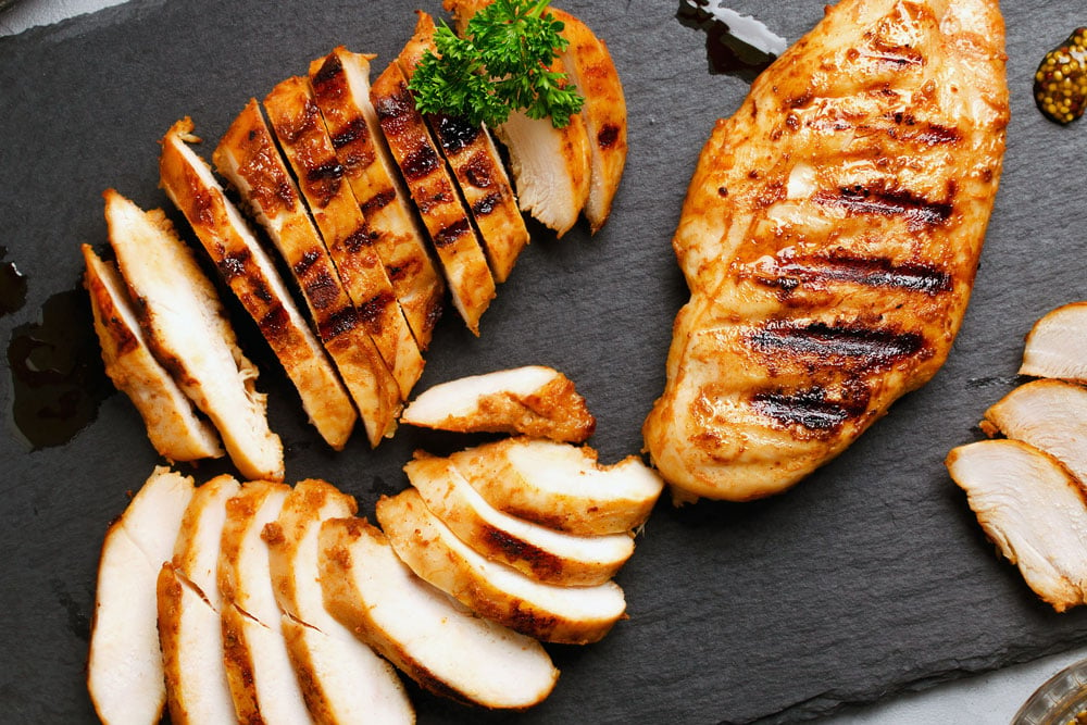 cooked chicken sliced on black food board